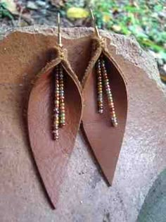 two pairs of brown leather earrings with beaded beads hanging from them on top of a rock