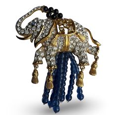 "Elizabeth Taylor Elephant Walk Brooch for Avon -- 1993 \"Elizabeth Taylor loves Indian jewelry. One of her favorite motifs is the elephant. an Indian symbol of good luck and new beginnings. These playful elephants glisten  with sparkling crystals and are showered by cascades of sapphire blue glass beads. On the pin, a golden tassels dangle from the toes of this magnificent creature who dances in delight at his own elegance.\" --Avon Circa: 1993" Luxury Ornate Collectible Brooches, Luxury Antique Blue Brooches, Elizabeth Taylor Jewelry, Indian Symbols, Luxury Gold-tone Jewelry Brooch, Elephant Brooch, Luxury Victorian Gemstone Brooch, Elephant Walk, Crystal Wine Glasses