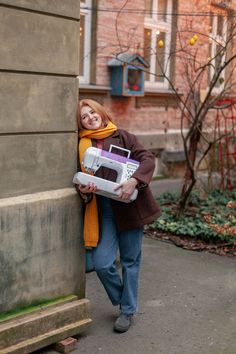 a woman leaning against a wall holding a white and purple object in her hands,