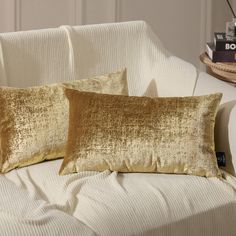 two gold pillows sitting on top of a white couch