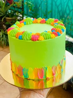 a hand holding a green cake with colorful frosting