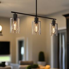 three lights hanging from a ceiling in a living room next to a dining room table