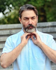 a man standing in front of a wooden bench with his hands on his chest and looking at the camera