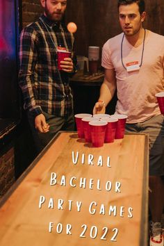 two men standing next to each other at a table with red cups in front of them