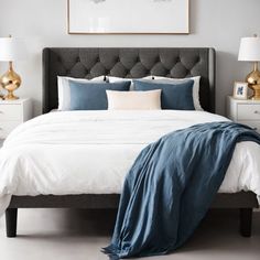 a bed with white sheets and blue blankets in a gray room next to two nightstands