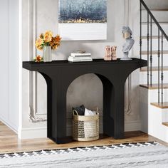 a black console table in the middle of a room with stairs and flowers on it