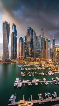 boats are docked in the water near tall buildings and skyscrapers at dusk, with dark clouds overhead