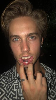 a young man with blue eyes and piercings on his teeth is posing for the camera