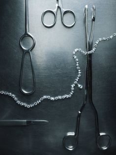 two pairs of scissors and a chain on a metal surface, with beads attached to them