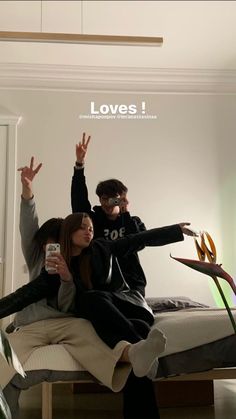 two people sitting on a bed with their arms in the air and one person taking a selfie