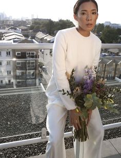 a woman holding a bouquet of flowers on top of a building with buildings in the background