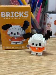 a lego figurine sitting next to a book on a wooden table with pens and pencils