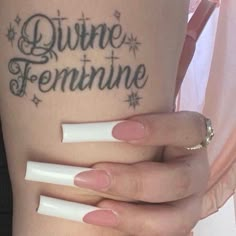 a woman's legs with white nails and tattoos on her leg, which reads divine feminine