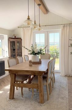 a dining room table with chairs and a vase on it's centerpiece in front of a window