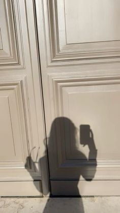 the shadow of a person holding a cell phone in front of a door with white paneling