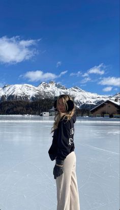 a woman standing on top of an ice covered field with mountains in the back ground