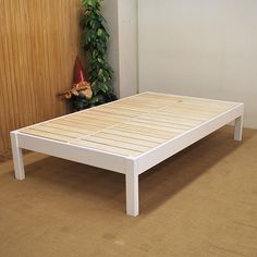 a white bed frame sitting on top of a wooden floor next to a potted plant