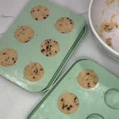 two green trays filled with chocolate chip cookies next to a white bowl full of batter