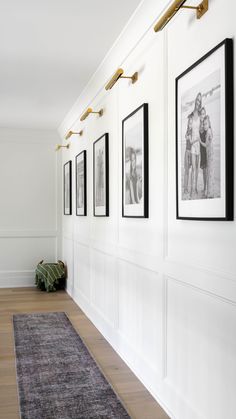 a long hallway with white walls and pictures on the wall, along with a rug