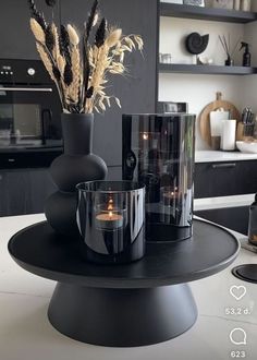 a black table with two vases and some candles on it in front of a kitchen