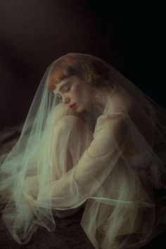 a woman wearing a veil with her head resting on her hands, in front of a dark background