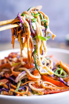 a bowl filled with noodles and vegetables being held by chopsticks