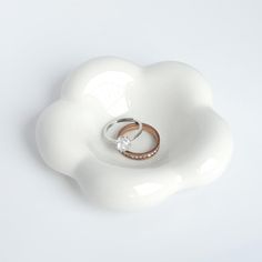 two wedding rings sitting on top of a white flower shaped dish with a diamond in the middle