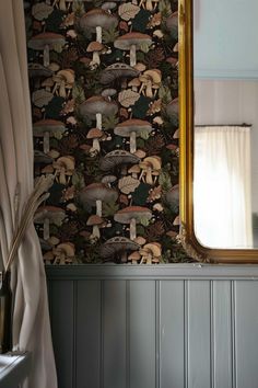 a mirror sitting on top of a wooden table next to a wallpaper covered in mushrooms