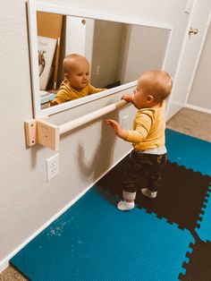 a small child standing in front of a mirror on the floor next to a blue mat