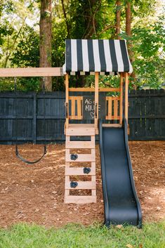 a black and white striped awning on top of a wooden slide in the grass