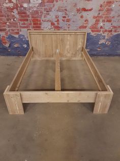 a wooden bed frame sitting on top of a cement floor next to a brick wall