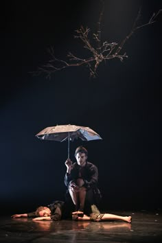 a woman sitting on the ground with an umbrella over her head and another person laying down behind her