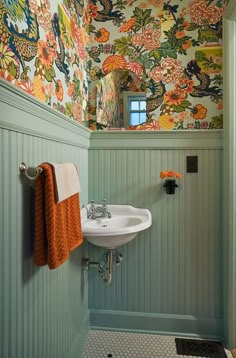 a bathroom with floral wallpaper and colorful towels hanging on the rack above the sink