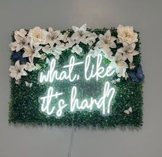 a neon sign that says what's like it's hard? surrounded by flowers