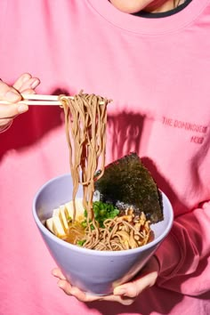 a person holding a bowl of noodles with chopsticks in their hand while eating it