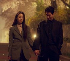 a man and woman holding hands walking down the street at night with trees in the background