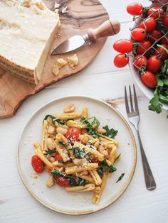 a white plate topped with pasta and spinach next to a bowl of tomatos