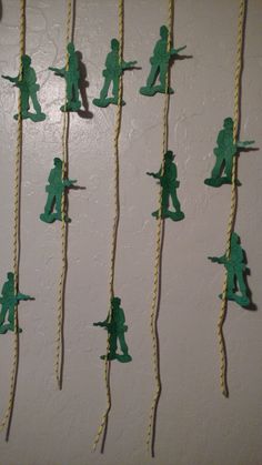 some green paper soldiers are hanging on the wall with string attached to each one's sides