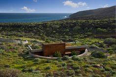 an aerial view of a house in the middle of a grassy area with water and mountains in the background