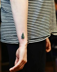 a small pine tree tattoo on the left wrist and right hand is shown in front of a woman's arm