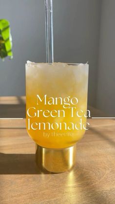 a glass filled with lemonade sitting on top of a wooden table next to a plant