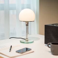 a lamp sitting on top of a white table next to a cup and cell phone