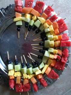 a platter filled with watermelon, blueberries and pineapples on skewers