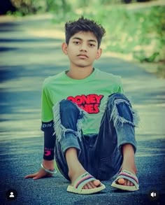 a young boy sitting on the side of a road with his legs crossed in front of him