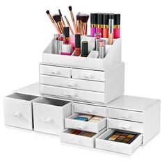 an assortment of makeup and eyeliners in white drawers on top of each other