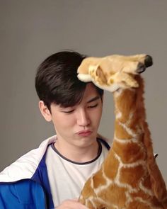 a young man holding a stuffed giraffe up to his head and looking at it