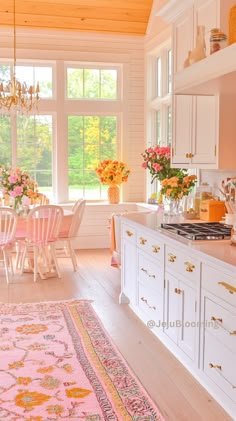 a kitchen filled with lots of white furniture and flowers on top of a counter next to a window