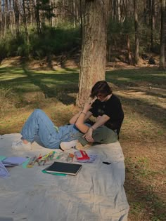 a woman sitting on the ground next to a tree with her laptop and other items