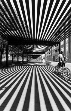 a man riding a bike down a street next to tall buildings with striped coverings