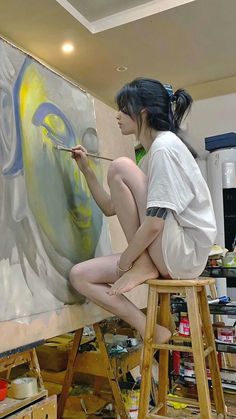 a woman is sitting on a stool painting